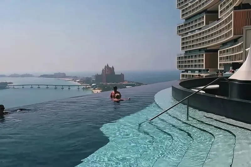 Купальщики в панорамном бассейне Atlantis The Royal с видом на Пальм Джумейра