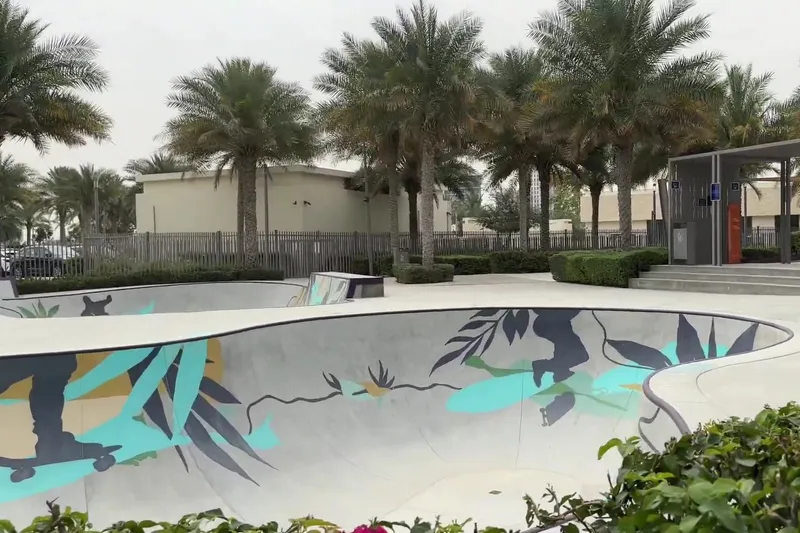 Бетонная площадка скейт-парка в Dubai Hills Park с яркими синими рисунками в окружении пальм.