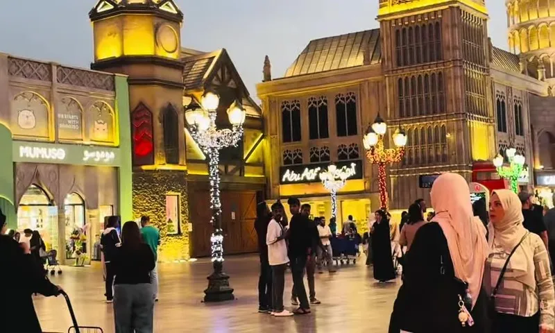 Оживленная улица Global Village с копиями Биг-Бена и Пизанской башни, украшенная декоративными фонарями в вечернее время.