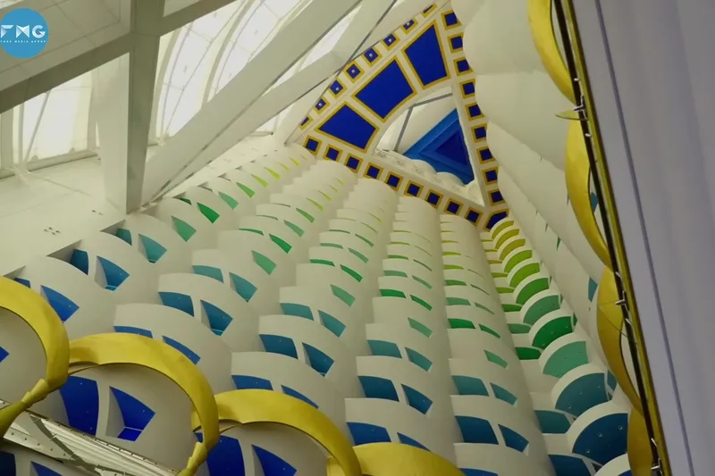 Вид снизу вверх на массивный атриум Burj Al Arab с разноцветными ярусными балконами синего, зеленого и желтого цветов.