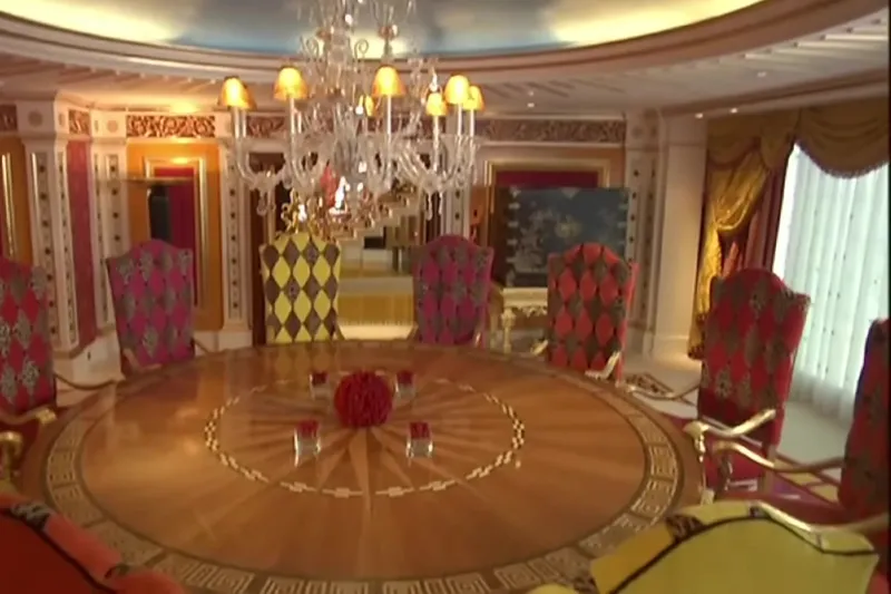 Интерьер столовой в номере Burj Al Arab с большим круглым деревянным столом, разноцветными стульями и массивной хрустальной люстрой.