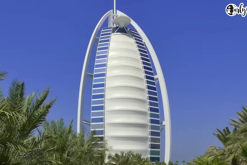 Полный вид на фасад отеля Burj Al Arab с его характерными белыми панелями на фоне ясного синего неба.