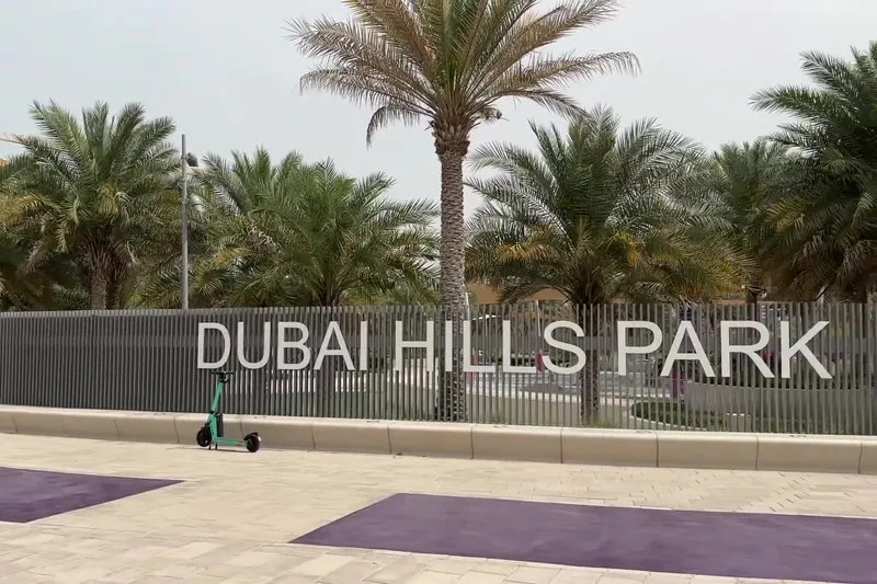 Вход в Dubai Hills Park с пальмами и электросамокатом