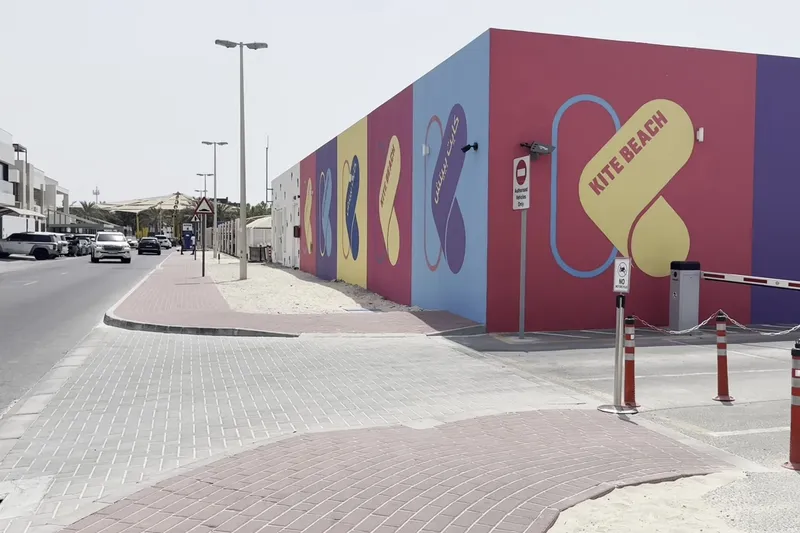 Яркая настенная роспись со стилизованной надписью Kite Beach в розовых, желтых и синих цветах.