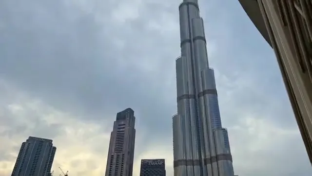 Вид снизу на фасад небоскреба Бурдж-Халифа, уходящий в облака и отражающий дневной свет.