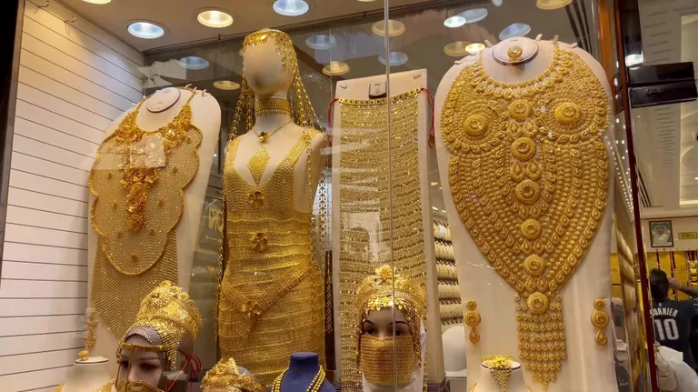 Манекены в витрине демонстрируют массивные золотые украшения, покрывающие грудь, и сложные изделия из драгоценного металла.