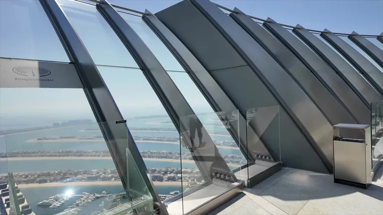 Открытая смотровая площадка с наклонными стеклянными панелями, обеспечивающими панорамный вид на Дубай и залив.