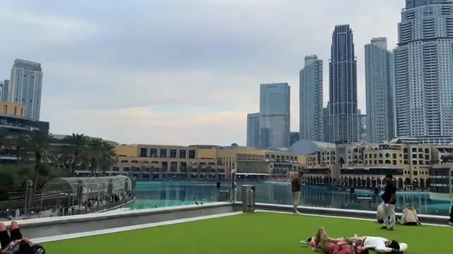 Отдыхающие на зеленой террасе с видом на бирюзовые воды озера и плотную застройку центра города.