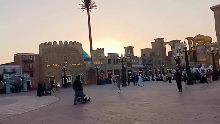 Центральная площадь с традиционной ближневосточной архитектурой и ветряными башнями в лучах заходящего солнца.