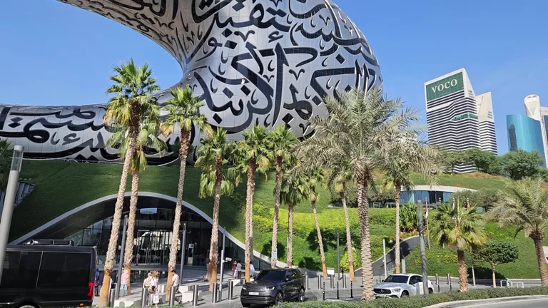 Главный вход в музей в окружении пальм, рядом с которым находятся посетители и автомобили.