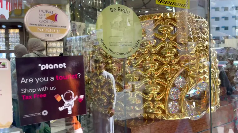 Массивное золотое кольцо с крупными прозрачными камнями и сложным узором, выставленное в витрине магазина.