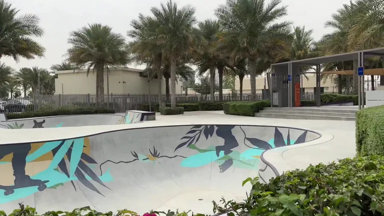 Бетонная площадка скейт-парка в Dubai Hills Park с яркими синими рисунками в окружении пальм.