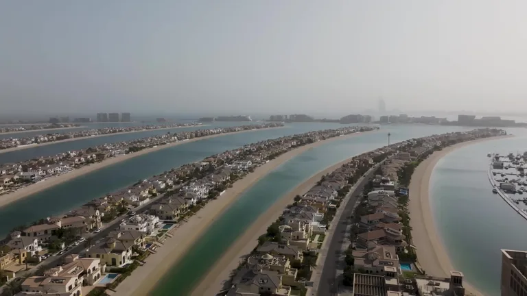 Вид сверху на искусственный остров Палм-Джумейра с рядами частных вилл, пляжами и бирюзовой водой.