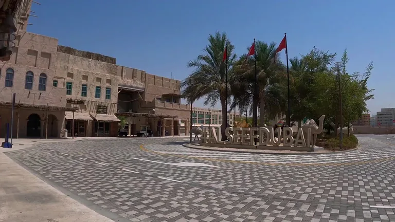 Главная площадь у входа в район Al Seef с традиционными эмиратскими зданиями, флагами и скульптурной вывеской.