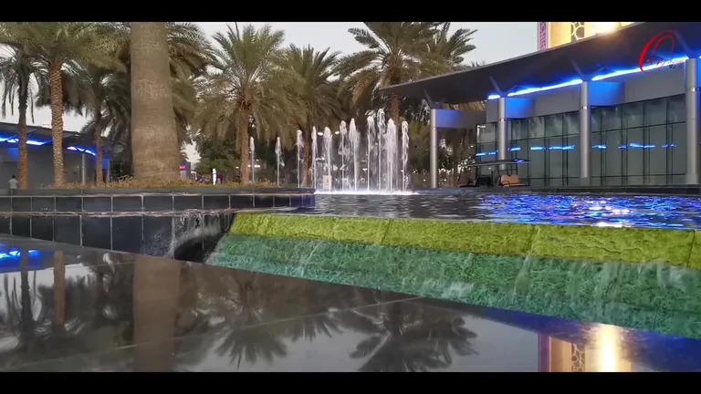 Декоративный фонтан с каскадным водопадом на территории парка Забиль в окружении пальм и зданий.