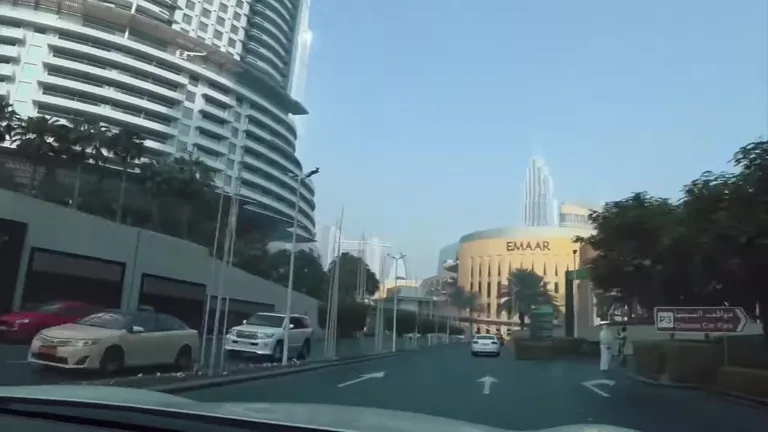 Вид из автомобиля на подъезде к Dubai Mall с изогнутым фасадом высотного здания и комплексом Emaar.