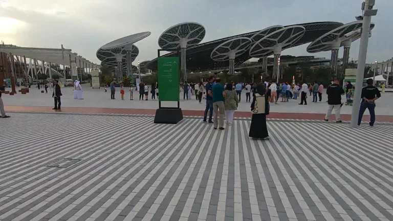 Large solar panel trees and striped pavement with visitors at the Terra Sustainability Pavilion.