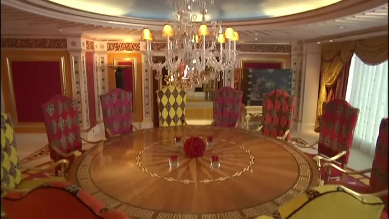 Обеденная зона в королевском люксе с массивным столом, яркими стульями и хрустальной люстрой под расписным потолком.