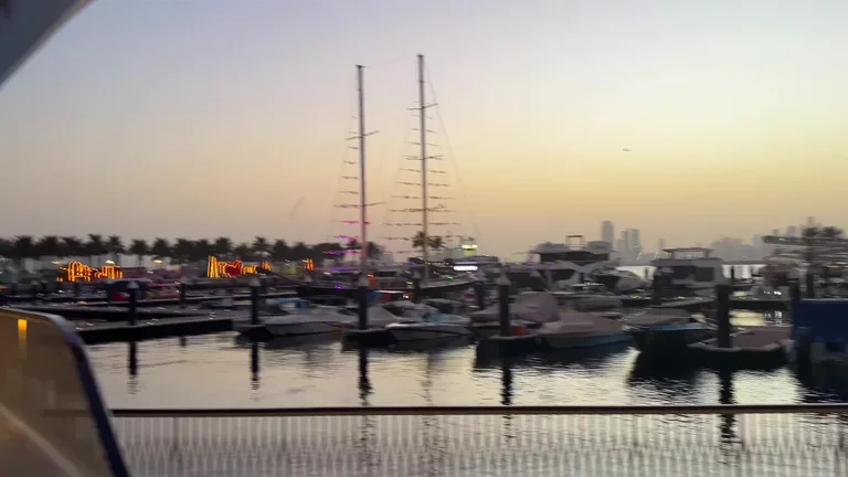 Вид на пристань с пришвартованными лодками в сумерках на фоне отдаленных очертаний Бурдж-Халифа и центра города.