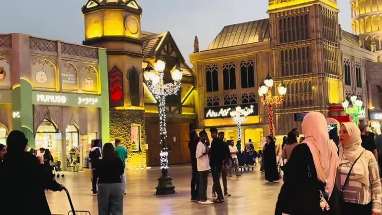 Оживленная аллея парка с копиями Биг-Бена и Пизанской башни на заднем плане в вечернее время.