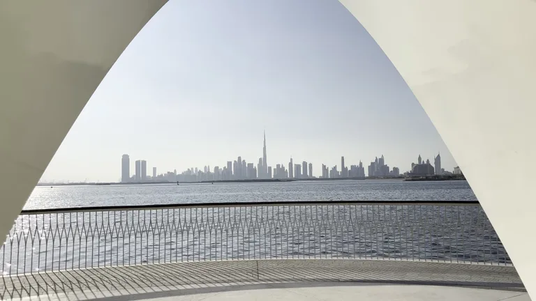 Вид на небоскребы Дубая через белую треугольную архитектурную раму, установленную на смотровой площадке набережной.