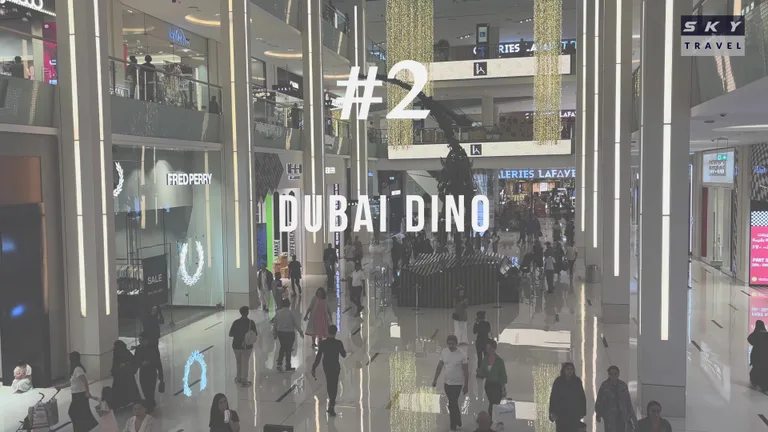 Многоуровневый атриум Dubai Mall с люксовыми магазинами и массивным скелетом динозавра, расположенным прямо в центре зала.