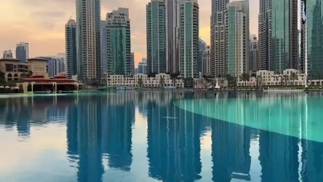 Панорама небоскребов Дубая, отражающихся в спокойных водах искусственного озера во время заката.